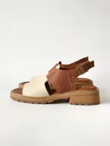 Sandalias de cuero combinadas en color marrón y crudo, con suela track y taco bajo. Tienen tira ajustable con hebilla en el talón.