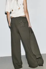 Pantalón de tiro medio con pierna ancha, confeccionado en tejido lavado. Presenta cintura elástica ajustable con cordones, bolsillos laterales y bolsillos traseros decorados con estrellas y aplicaciones de tachas. El diseño cuenta con terminaciones desflecadas en el ruedo.