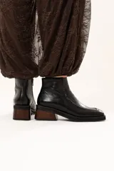 Bota de cuero color chocolate con horma cuadrada, taco bloque de madera y plataforma. Presenta cierre lateral interno y detalle de ribete en la capellada.