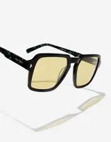 Lentes de sol Hawkers modelo Lash con armazón negro de frente cuadrado y patillas con estampado de mármol en tonos verdes. Presentan cristales amarillos y detalles metálicos en las esquinas.