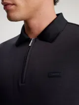 Chomba Calvin Klein negra de algodón, con cuello polo y media cremallera. Tiene mangas cortas y parche de goma con el logo de la marca en el pecho.