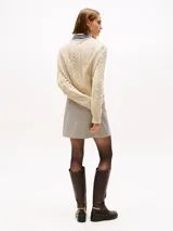 Sweater de punto color beige, con cuello en V ribeteado con franjas azul marino y blanco. Presenta tejido cableado (trenzas) en el frente y mangas largas.