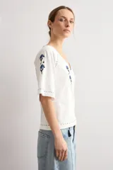 Remera blanca de manga corta con escote en V, decorada con delicados bordados florales en azul oscuro en el pecho, hombros y mangas.