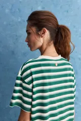 Remera de calce relajado con diseño a rayas horizontales blancas y verdes, hombros caídos y mangas amplias con vuelta. Presenta cuello redondo y ruedo trasero levemente más largo.