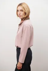 Remera de manga larga en color rosado, con cuello redondo y cierre frontal parcial con botones. Presenta un diseño de corte recto y estilo minimalista.