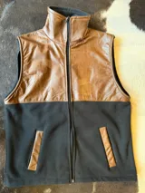 Chaleco bicolor con diseño combinado de cuero marrón en la parte superior y tejido polar negro en la parte inferior, cuello alto, cierre frontal y bolsillos ribeteados.