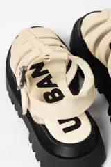 Sandalia tipo gladiadora con plataforma track negra. Presenta un diseño bicolor con tiras delanteras en color amarillo neón y talón con tira ajustable en color beige. Incluye hebilla metálica negra.