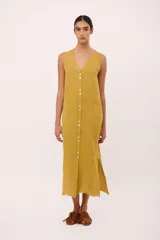 Vestido midi sin mangas de color amarillo mostaza, con escote en V y cierre frontal de botones. Presenta tajos laterales y terminación desflecada en el ruedo.