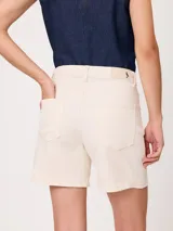 Short de denim elastizado de tiro alto, color beige, con bolsillos delanteros y traseros, y cierre frontal con botón y cremallera.