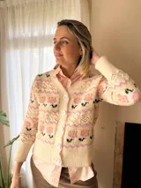 Cárdigan de punto con diseño jacquard floral en tonos rosa, amarillo y verde sobre base color crema. Presenta cuello en V, cierre frontal con botones grandes y detalles de calados en el tejido.
