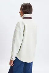 Campera de sherpa color crudo con cuello alto, cierre frontal completo y detalles en color bordó. Presenta un bolsillo frontal con cierre y dos bolsillos laterales, todos con terminaciones en contraste.