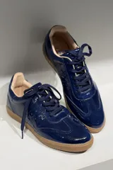 Championes de cuero vacuno con acabado brillante tipo charol, color azul marino, con cordones al tono y suela de goma color caramelo.