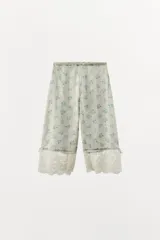 Pantalón bombacho de tiro medio y cintura elástica, confeccionado en viscosa con estampado floral y rayas sutiles. Presenta bajo ajustable con lazada y aplicación de encaje contrastante en el ruedo.