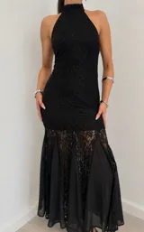 Vestido largo negro de encaje y tela translúcida, con cuello halter alto y diseño ajustado que se ensancha en la parte inferior con paneles de gasa.