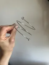 Brazalete rígido plateado con forma de espiral, con dos circonias engarzadas en los extremos.