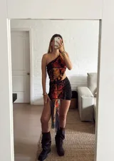 Vestido corto con diseño asimétrico de un solo hombro, con estampado de alas de mariposa en tonos naranja y negro. Presenta un corte cut-out en la cintura y un detalle de tela drapeada que cae desde la cintura hacia el ruedo.