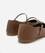 Zapatilla plana de cuero marrón estilo Mary Jane, con puntera cuadrada y tira fina con hebilla metálica dorada sobre el empeine.