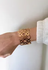 Brazalete ancho de diseño calado con formas circulares entrelazadas de diferentes tamaños, acabado en tono dorado brillante.