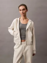 Buzo con capucha y cierre frontal completo, color beige jaspeado, confeccionado en suave fleece de mezcla de algodón y poliéster. Presenta bolsillos laterales y el logo Archive de Calvin Klein bordado en el pecho.