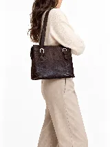 Cartera de hombro de cuero vacuno marrón con textura animal print en relieve, diseño estructurado, asas largas y detalles de hebillas metálicas plateadas en el frente.