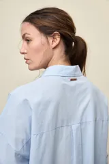 Camisa celeste de corte oversize, con mangas largas, cuello camisero y cierre frontal de botones.