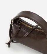 Cartera pequeña de diseño estructurado color marrón, con asa corta fija y correa larga desmontable. Cuenta con cierre superior de cremallera y detalle de tiras decorativas en el lateral.