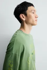 Camiseta de manga larga con corte relajado y cuello redondo, confeccionada con un acabado de efecto lavado. Presenta un estampado frontal con tipografía gótica y números en contraste.