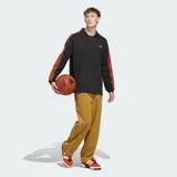Camisa polo Adidas de manga larga en color negro, con cuello clásico y las icónicas tres tiras naranjas en las mangas. Presenta el logotipo del trébol bordado en naranja en el pecho con la inscripción 'Basketball'.