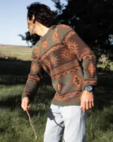 Buzo tejido de punto con diseño geométrico de estilo étnico en tonos verde, marrón y salmón. Presenta cuello redondo, puños y ruedo acanalados, con etiqueta de la marca Denali en el interior y en el frente.