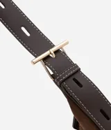 Cartera bandolera de formato media luna, confeccionada en material sintético efecto gamuza color marrón. Presenta correa larga ajustable con costuras a la vista y cierre superior con cremallera.