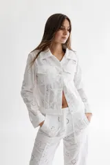 Campera blanca de lino con bordado calado, corte clásico de campera de jean, con cuello camisero, cierre frontal con botones de pasta color marfil, bolsillos de parche con solapa en el pecho y mangas largas con puños abotonados.
