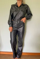 Mono largo negro de cuero sintético con textura de cocodrilo, cuello camisero, cierre frontal con botones, mangas largas con puños elásticos, bolsillos con solapa en el pecho y corte recto.