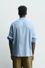 Camisa de corte relajado confeccionada en tejido fluido con mezcla de viscosa, color celeste. Presenta cuello solapa, manga larga con puños abotonados y cierre frontal de botones.