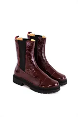 Bota tipo chelsea de cuero acharolado color bordó, con elásticos laterales negros y suela track dentada.