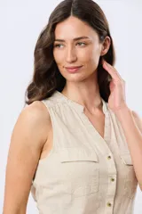 Musculosa de lino color beige, con cuello mao y escote en V, cierre frontal con botones y dos bolsillos plaqué con solapa en el pecho.