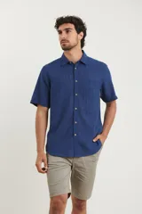 Camisa sport de manga corta, confeccionada en una mezcla de lino y algodón. Presenta cuello clásico, cierre frontal con botones de coco y un bolsillo en el pecho.