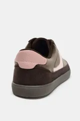 Zapatillas deportivas de estilo urbano, confeccionadas en una combinación de gamuza marrón oscuro y detalles en cuero rosado en el lateral y el talón. Presentan cierre mediante cordones al tono y suela de goma plana.
