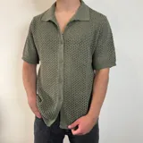 Camisa de tejido de punto calado en color beige, con cuello polo, cierre frontal de botones y mangas cortas.