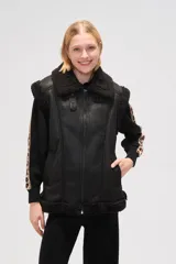 Chaleco de estilo aviador en color marrón, confeccionado en material tipo cuero con interior y bordes de corderito sintético en color crema. Presenta cierre frontal, cuello alto con tira de ajuste y bolsillos laterales.