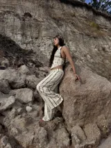 Top de cuello halter con escote en V profundo y bajo en punta. Presenta un diseño de rayas horizontales irregulares en color marrón sobre fondo beige y se ajusta mediante lazos en el cuello y la espalda.