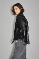 Campera de cuero sintético negro con acabado brillante, diseño tipo camisa con cuello clásico, cierre frontal con botones a presión y bolsillos delanteros. Cuenta con forro interior de algodón.