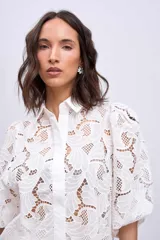 Camisa blanca de broderie con cuello clásico, mangas abullonadas 3/4 y cierre frontal con botones.