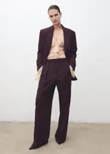 Pantalón de vestir bordó de tiro medio, con diseño wide leg, pinzas en la parte delantera, bolsillos laterales y cierre frontal con botón, gancho y cremallera.