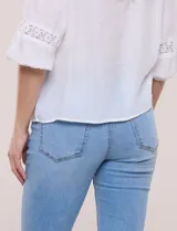 Blusa blanca de manga larga con escote en V y detalles de encaje en la botonera frontal, cuello y puños.