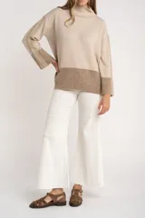 Sweater tipo polera de calce oversize, con diseño color block que combina tonos beige y marrón. Presenta cuello alto, mangas largas con puños acanalados y un panel inferior acanalado a juego.