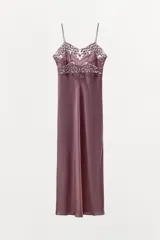 Vestido midi satinado de corte lencero, con escote en pico y tirantes finos. Presenta detalles de bordados florales y aplicaciones de encaje en la parte superior.