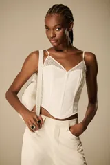 Corset estructurado de color blanco marfil (off-white), con inserciones de tejido calado en el escote y finos breteles ajustables. Cuenta con diseño de costuras entalladas y terminación curva en el bajo.