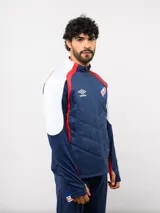 Buzo de entrenamiento Umbro del Club Nacional de Football, con cierre frontal parcial y cuello alto. Presenta un diseño con bloques de color azul, blanco y rojo, con panel frontal acolchado y mangas largas con aberturas para pulgares.