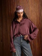 Camisa de raso color bordó, de corte holgado y diseño cropped. Presenta cuello clásico, cierre frontal con botones y mangas largas con puños abotonados.