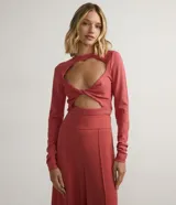 Blusa corta de tejido de punto color salmón, con cuello redondo, mangas largas, recortes frontales y detalle retorcido.